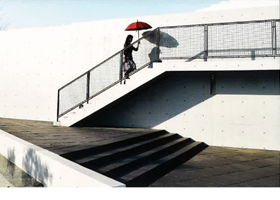 デジタルはじめました、さんの写真作品3です。真っ白な壁を背景に、赤い日傘をさして歩く女性が幻想的です。