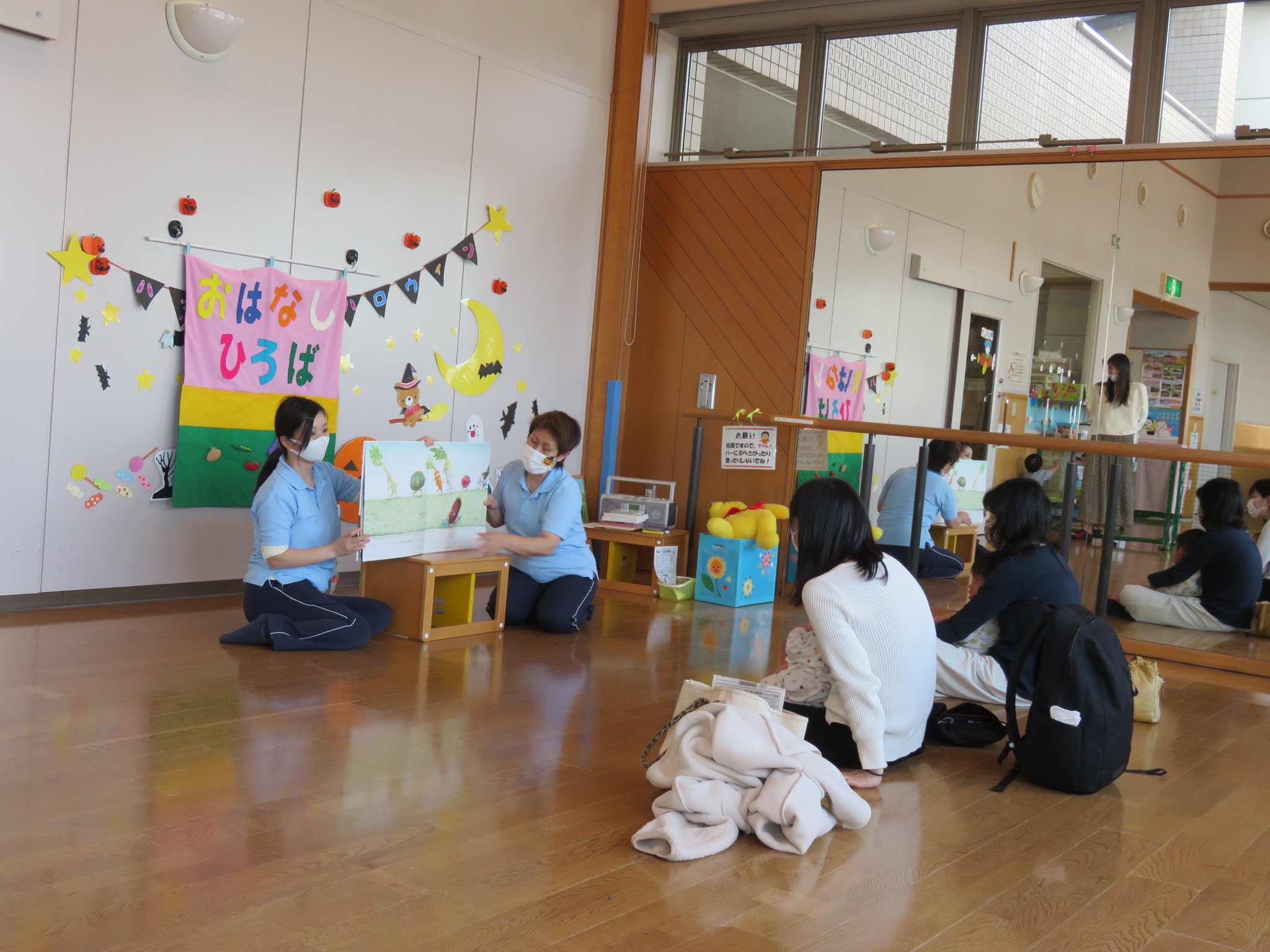 2組の親子の前で児童館職員が本を読み聞かせしている写真